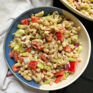Bowl of macaroni pasta salad with red bell peppers and celery and another bowl of it off to the side.