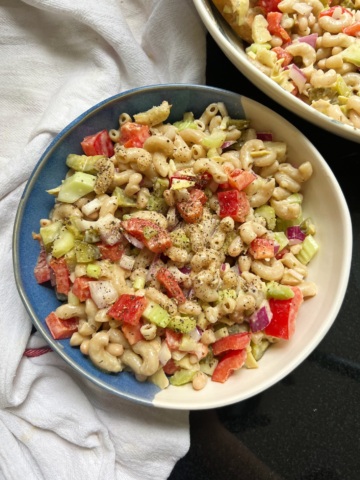 Bowl of macaroni pasta salad with red bell peppers and celery and another bowl of it off to the side.