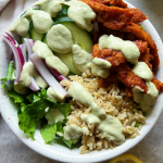 White bowl with BBQ soy curls, cucumber, romaine lettuce, red onion and rice with a creamy vegan ranch sauce on top.