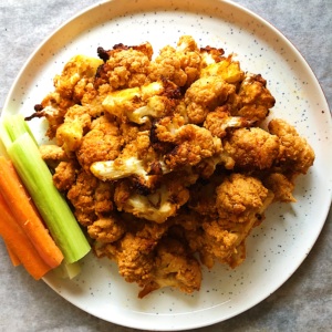 White plate with buffalo cauliflower wings on it with celery and carrot sticks on the side.