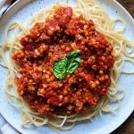 White plate with spaghetti pasta and lentil bolognese sauce on top with basil.