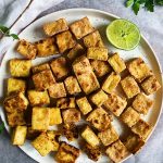 White background and plate with crispy garlic tofu on top with lime and cilantro in the corner.