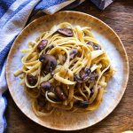 Plate of linguine with mushroom and lemon on a table with a blue and white table cloth