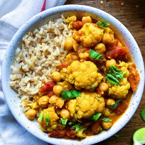 White bowl with rice on one side and cauliflower chickpea curry on the other side garnished with parsley