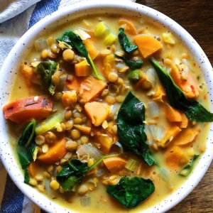 White bowl with creamy coconut lentil stew with sweet potatoes in it, lentils and spinach with a white and blue striped towel in the background.