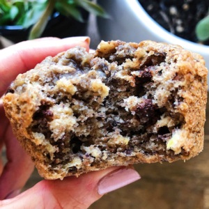 Hand holding a banana chocolate chip muffin with a bite taken out of it.