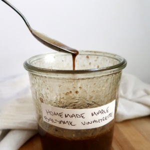 Spoon resting on a glass jar filled with homemade maple balsamic vinaigrette, with a white cloth in the background.