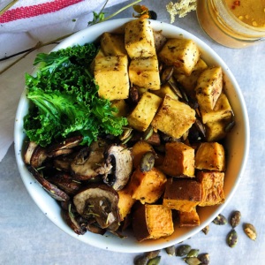 White background with kale, sautéed mushrooms, roasted sweet potato and Miso Sesame Tofu with a sauce on the side.