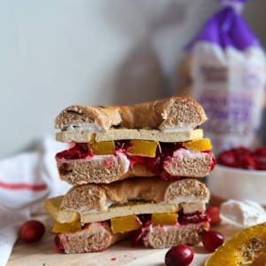 Bagel sandwich with sliced tofu, rosemary butternut squash and cranberry sauce on top of a cutting board.