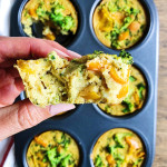 Muffin tin of vegan egg bites with broccoli and orange bell pepper. A hand holding half an egg bite.