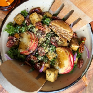 Bowl of salad with roasted tofu, apples and tongs in the bowl