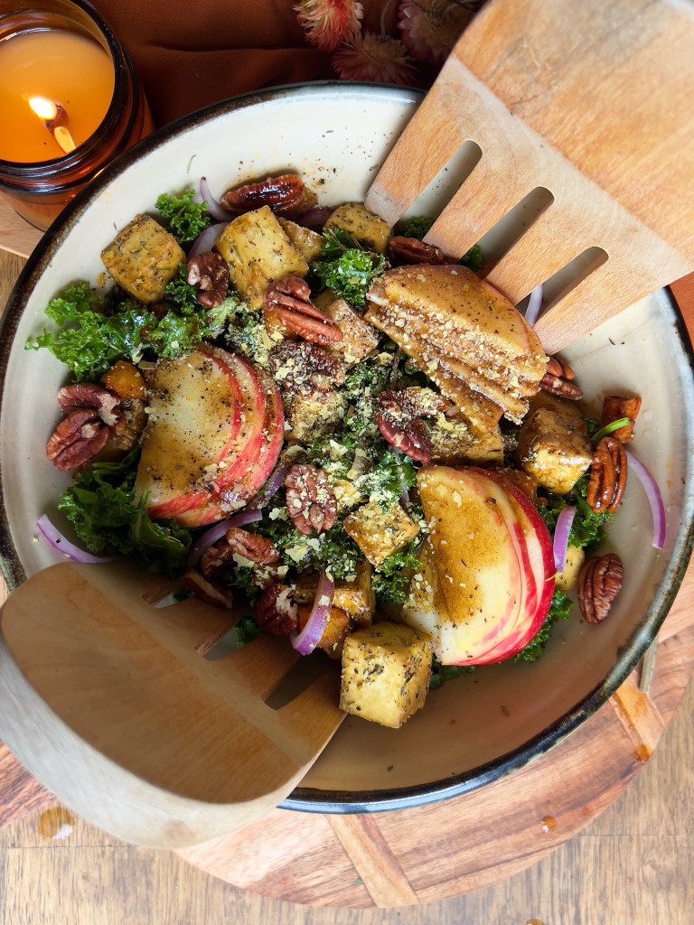 Bowl of salad with roasted tofu, apples and tongs in the bowl