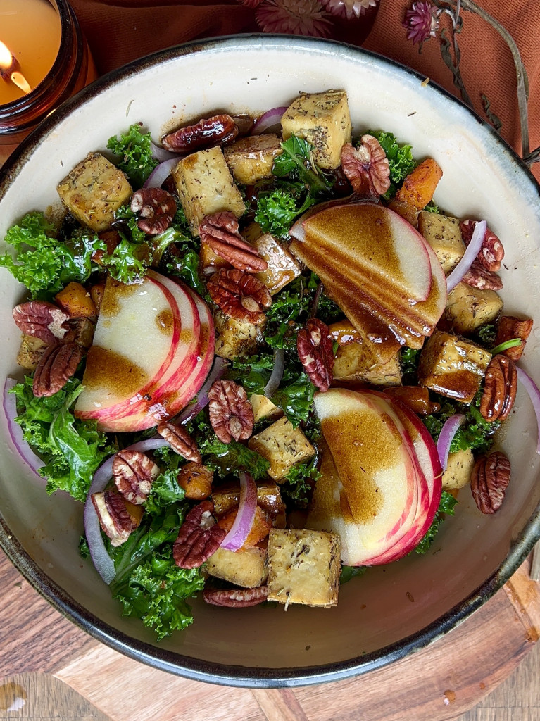Salad in a large white bowl with roasted tofu, pecans, red onion, sliced apple and salad dressing