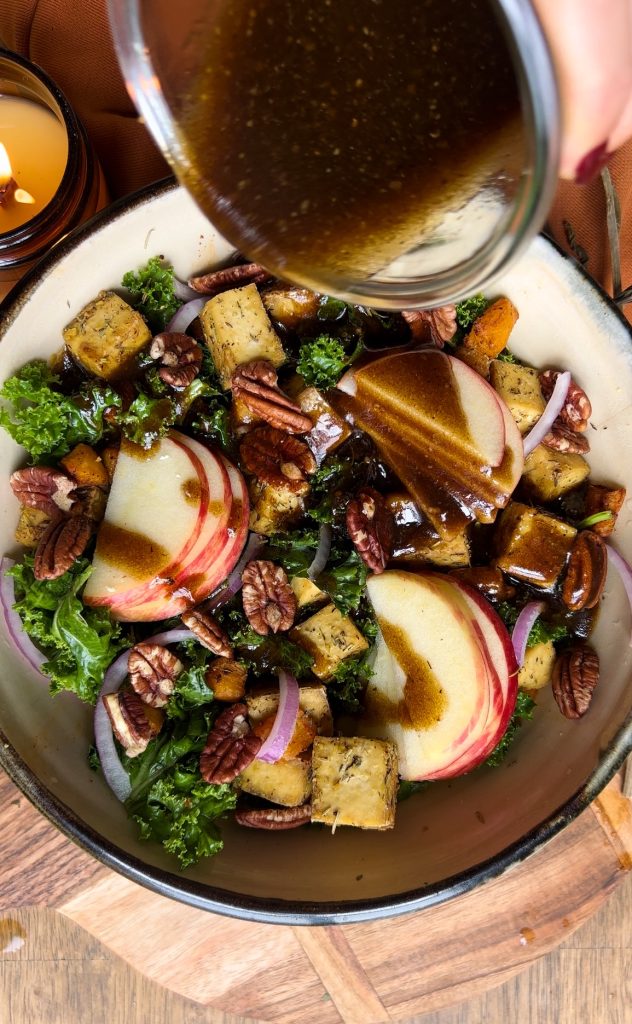 Salad with roasted tofu, sliced apple, red onion and pecans pouring salad dressing on top
