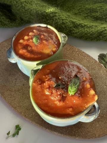 Two bowls of vegan lasagna soup on a white background garnished with basil.