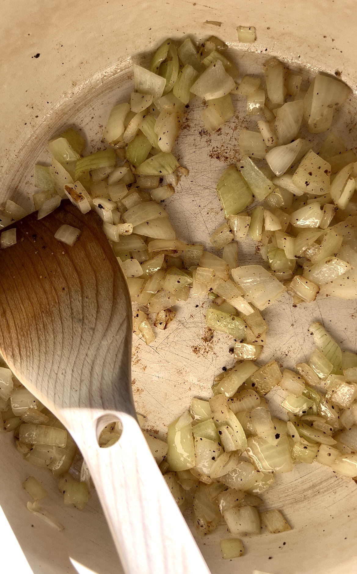 Diced onions in a large pot being sauteed with a wooden spoon.