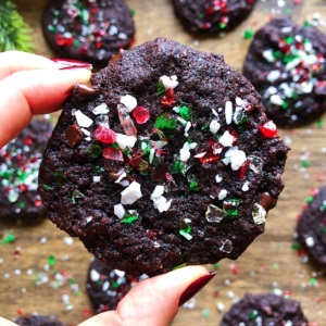 Hand holding a vegan candy cane chocolate chip cookie with other cookies in the background