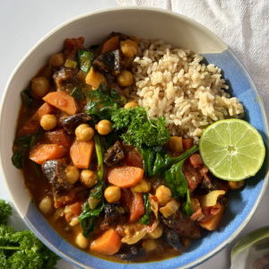 Blue and white bowl of spiced chickpea stew and brown rice with a lime wedge on the side.