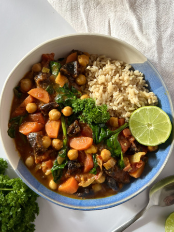Blue and white bowl of spiced chickpea stew and brown rice with a lime wedge on the side.