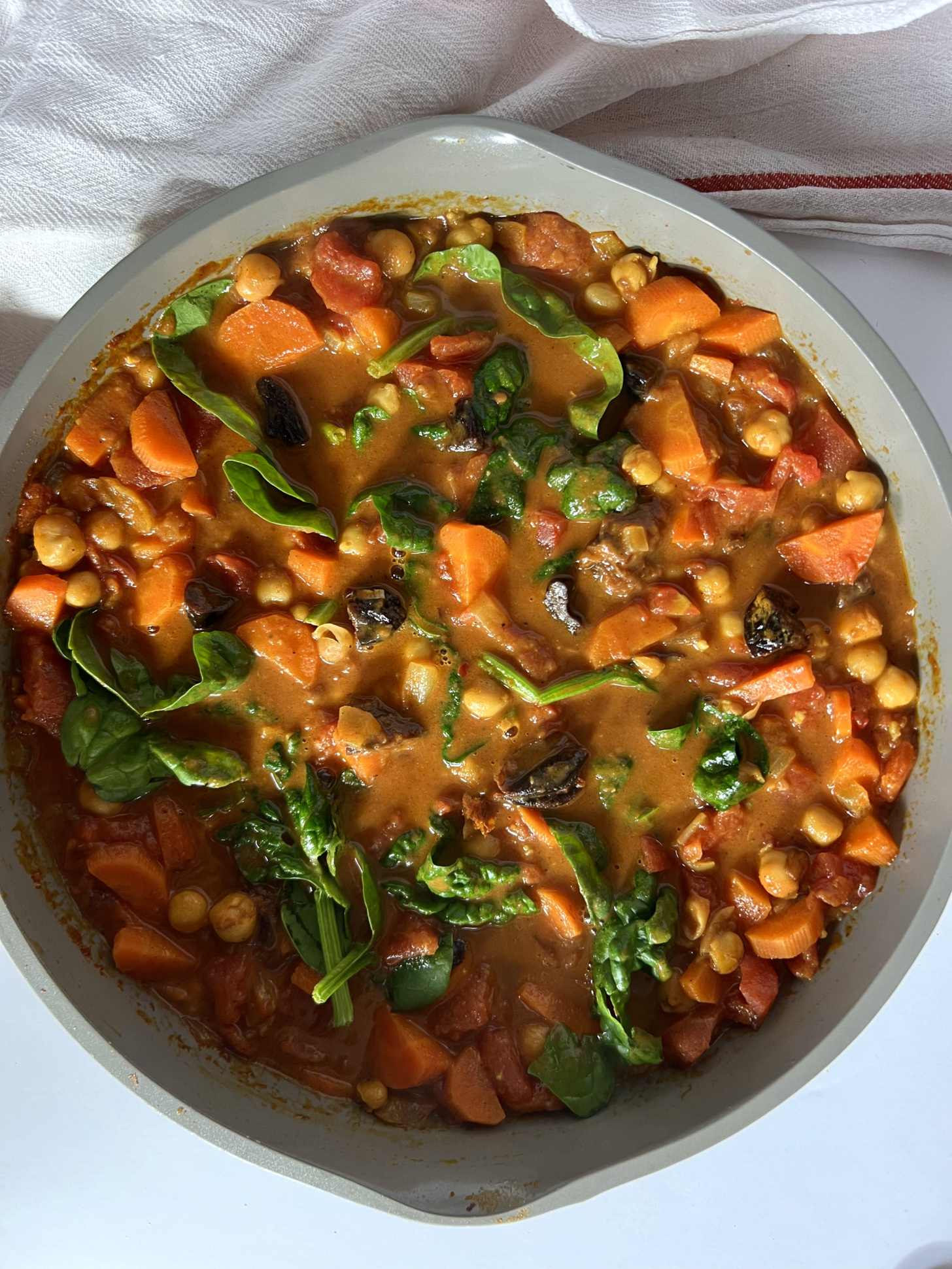 Pan with spiced chickpea stew with sliced carrots, chickpeas, and spinach.