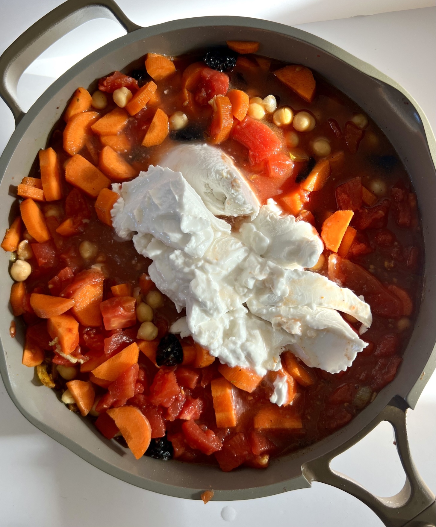 Pan with sliced carrots, canned tomatoes, chickpeas, prunes and canned coconut milk.