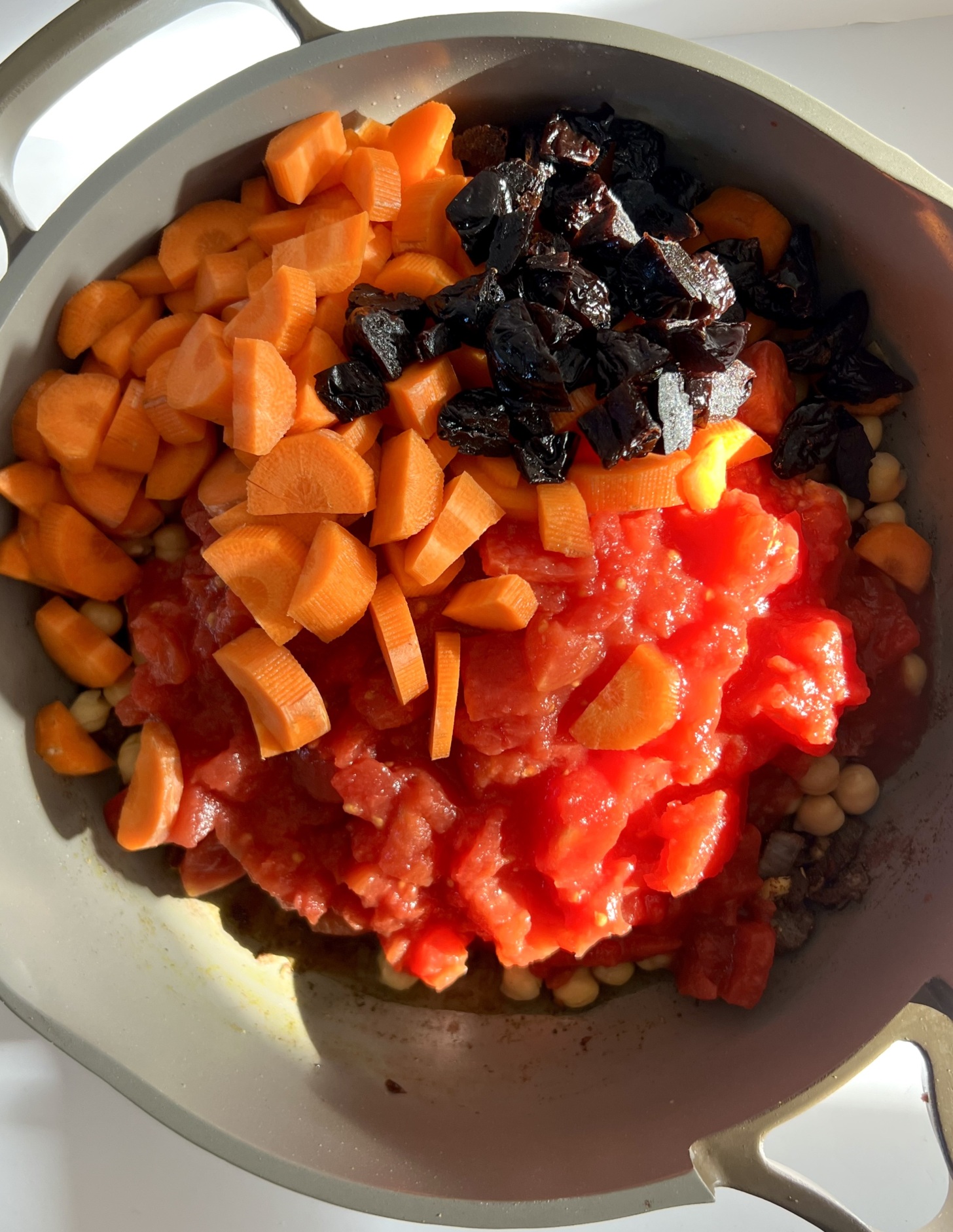 Pan with sliced carrots, canned tomatoes, chickpeas and prunes.
