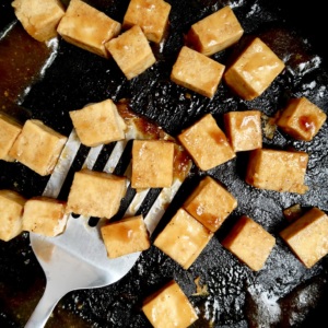 Pan with cubed tofu with teriyaki sauce and a spatula scooping some.