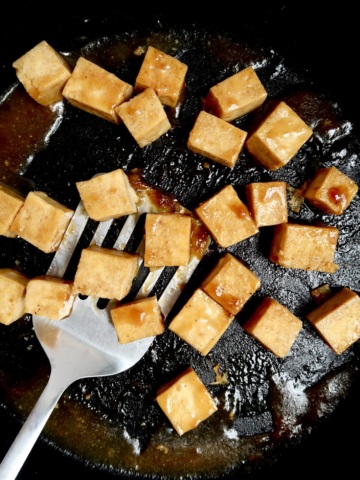Pan with cubed tofu with teriyaki sauce and a spatula scooping some.