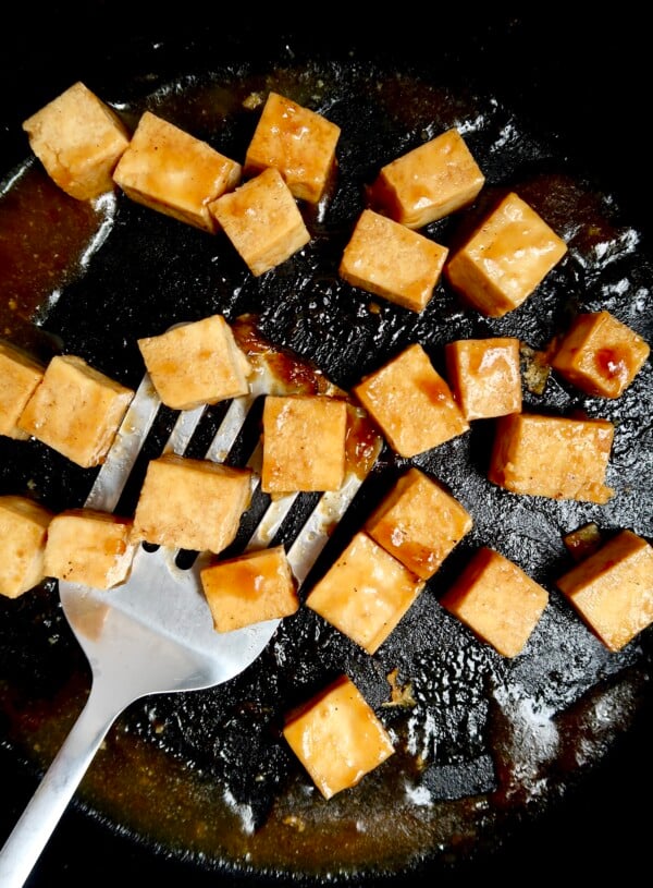 Pan with cubed tofu with teriyaki sauce and a spatula scooping some.
