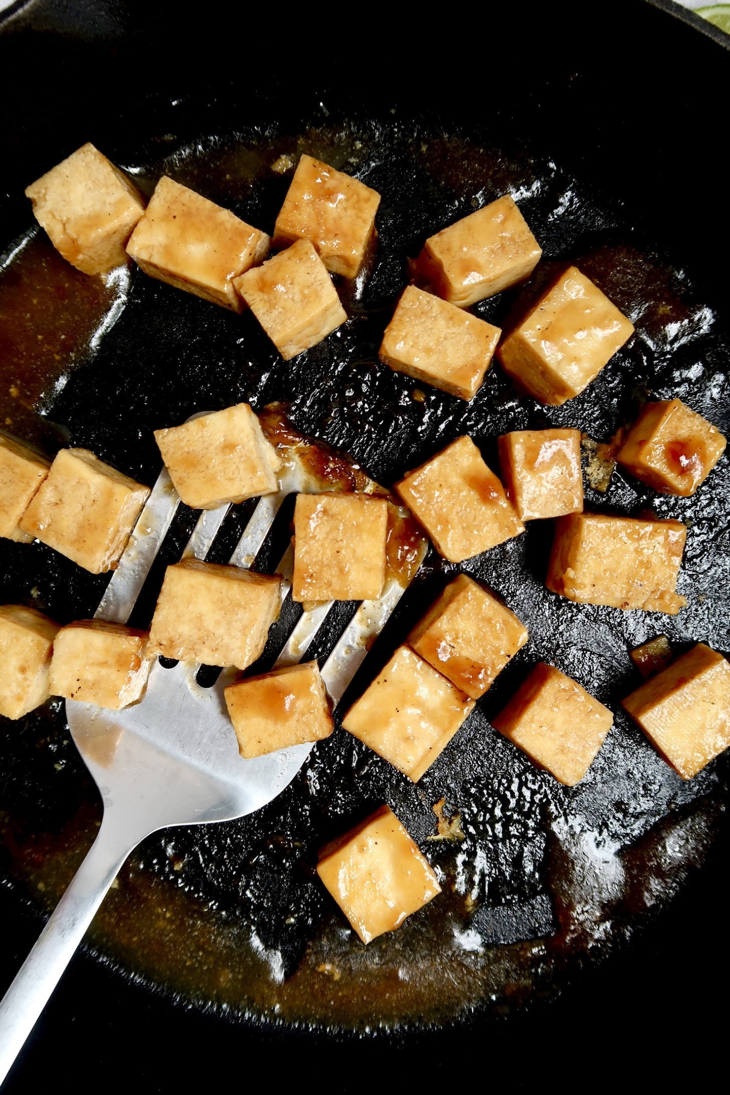 Pan with cubed tofu with teriyaki sauce and a spatula scooping some.