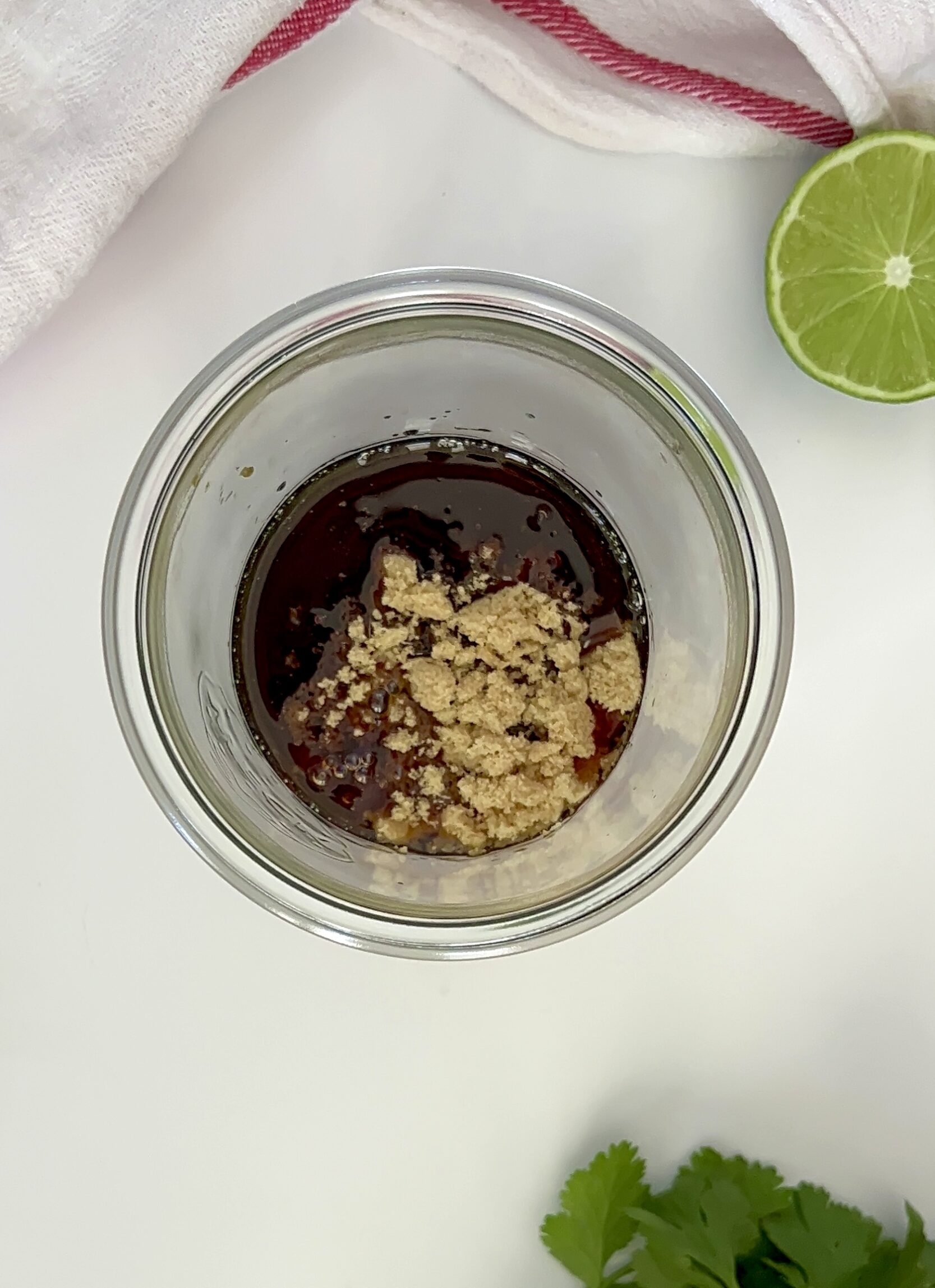 Mason jar with soy sauce and oil in it with brown sugar on top and a lime off to the side. 
