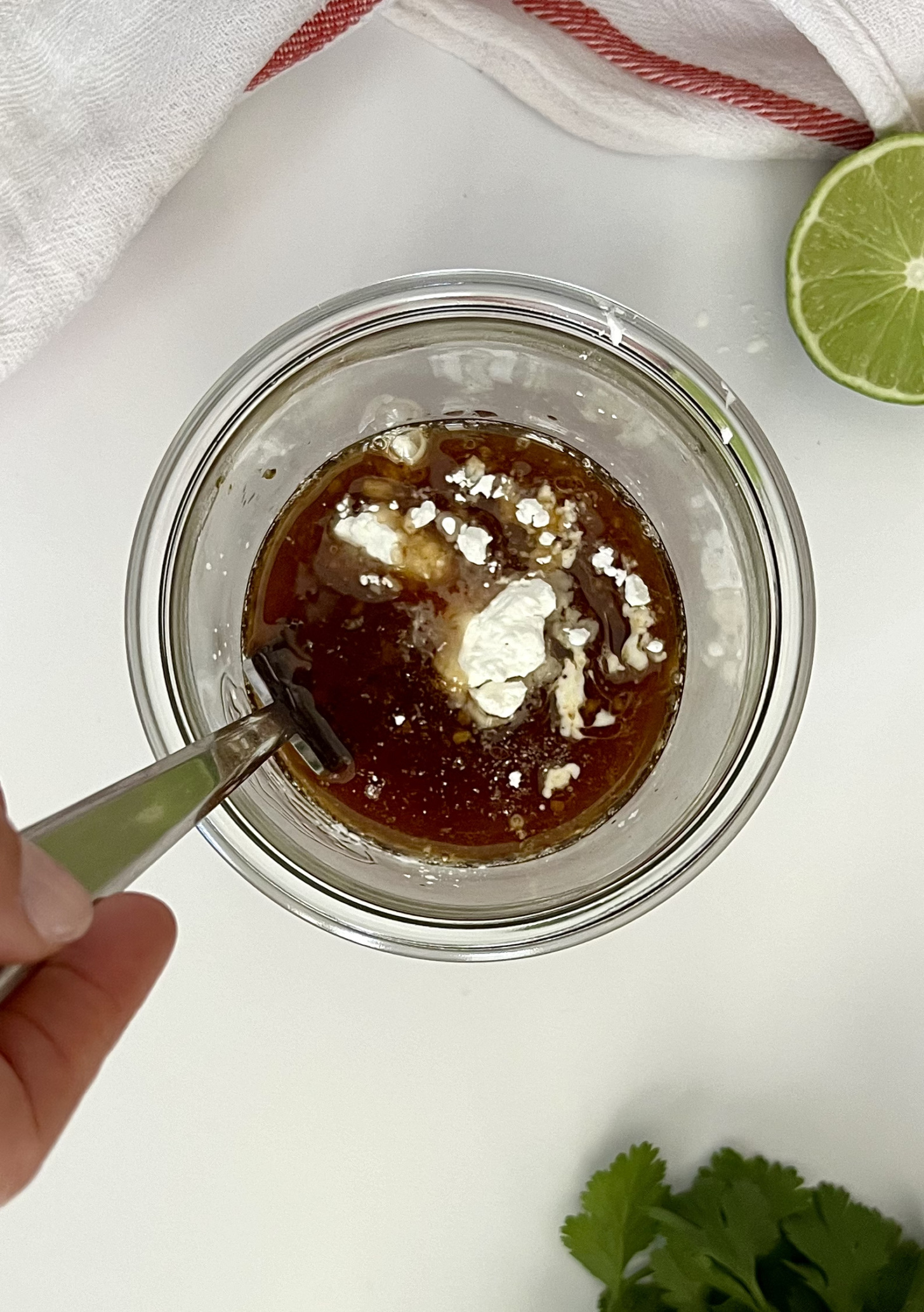 Mason jar with sauce ingredients and a fork inside to whisk and a lime for garnish.