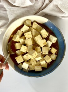 Cubed tofu in a blue and white bowl tossed in teriyaki sauce.