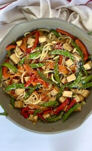 Teriyaki tofu, udon noodles and veggies in a pan with sesame seeds on top.