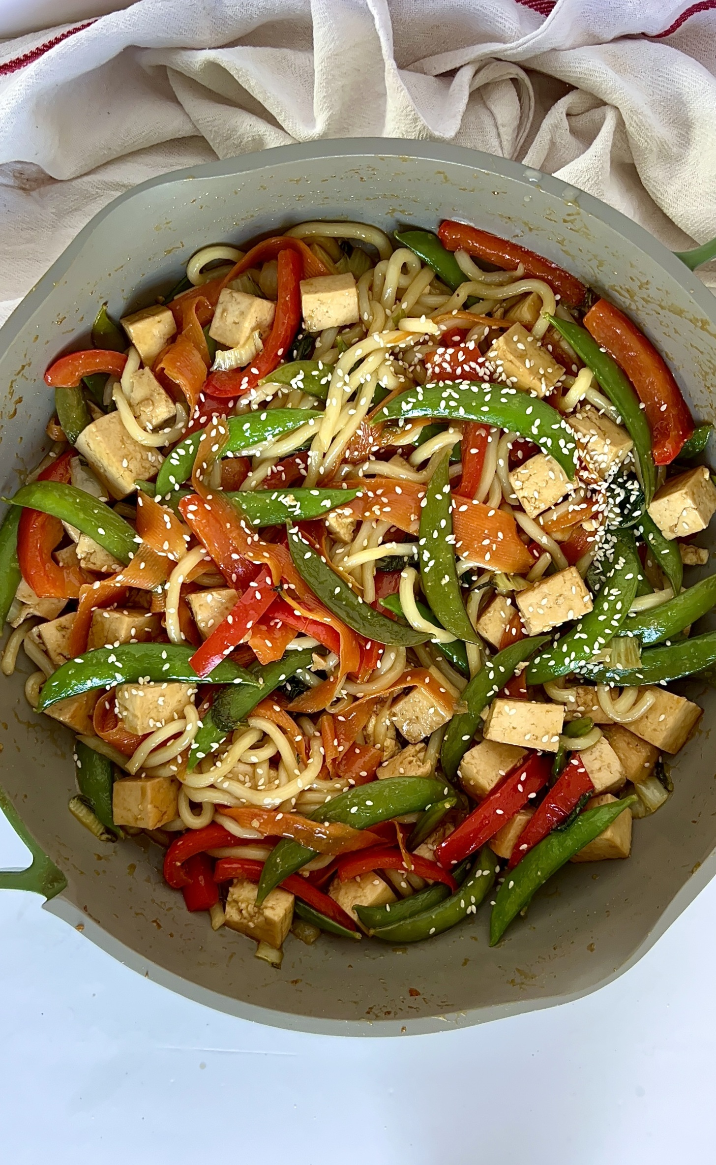 Pan with cubed tofu and veggies with udon noodles and sesame seeds on top.