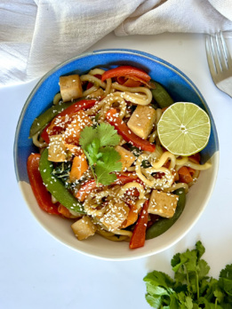 Udon noodle stir fry with tofu and vegetables in it with lime to garnish.