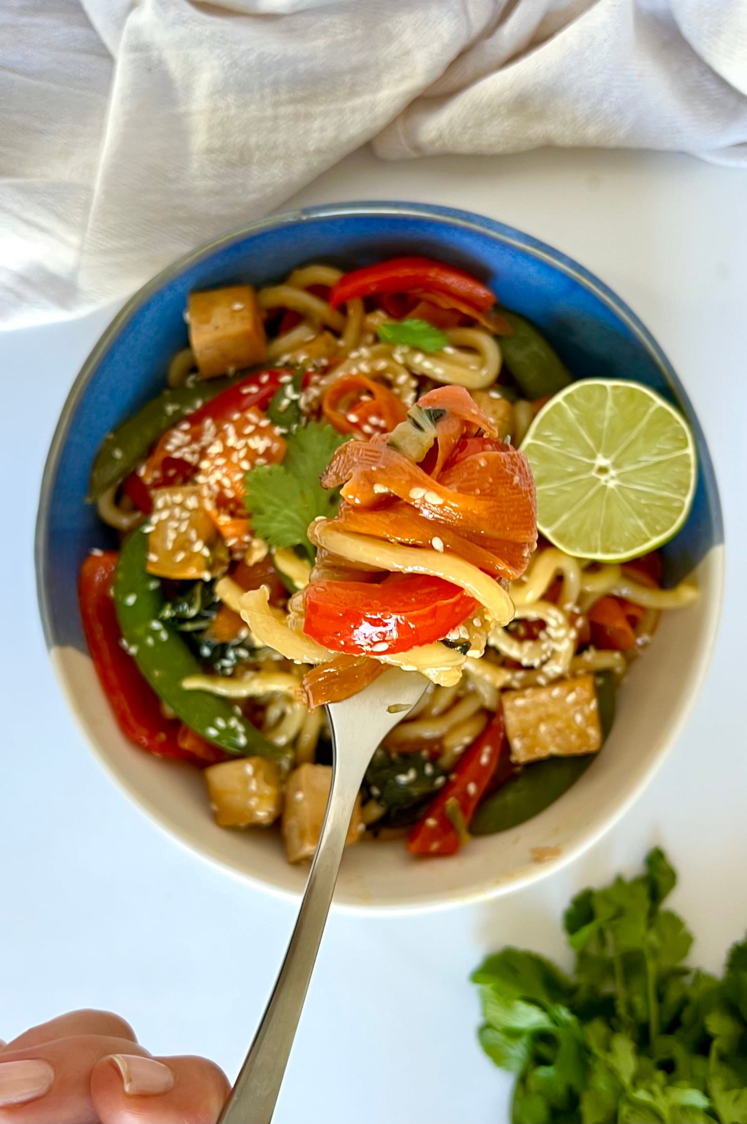 Blue and white bowl with udon noodle stir fry and veggies with tofu and lime.