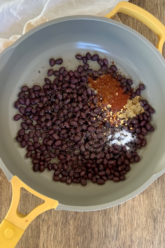 Pan of rinsed black beans with spices to the side that haven't been mixed in yet.