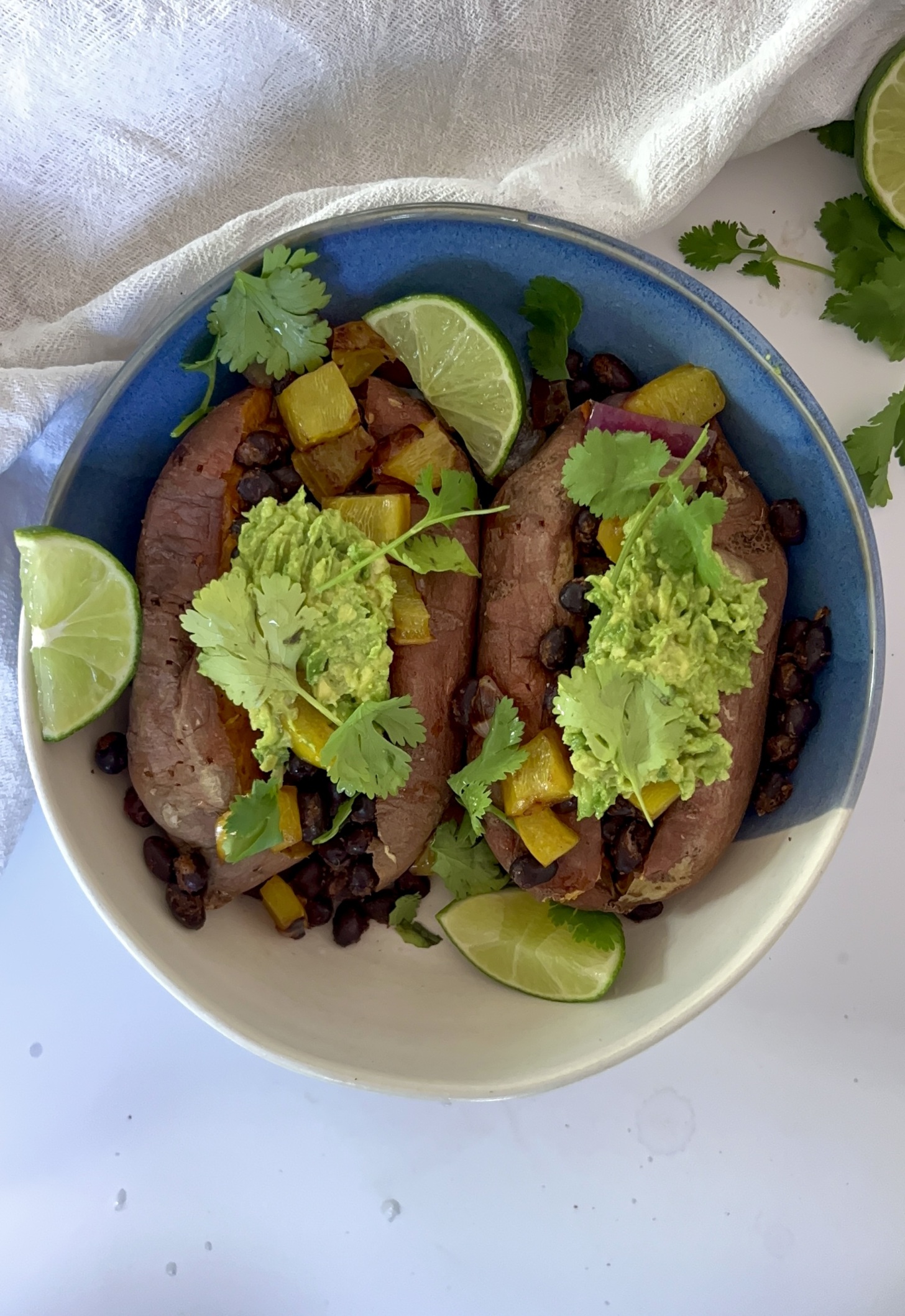 Bowl of baked sweet potatoes with black beans, bell pepper, mashed avocado and lime on the side