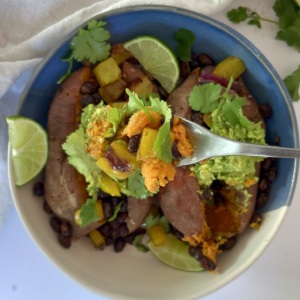 Bowl with a sweet potato with spiced black beans inside with guacamole and a fork.