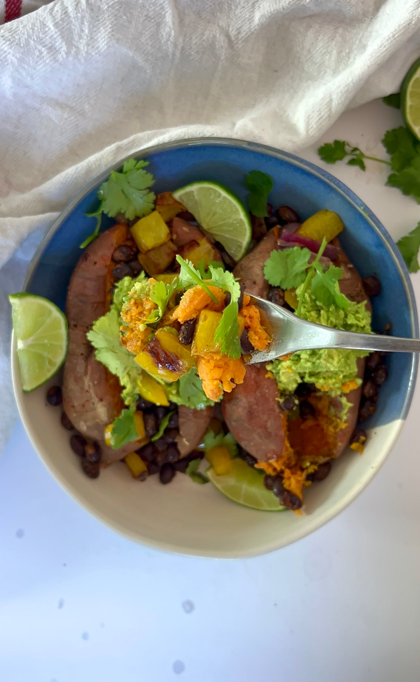 Bowl with a sweet potato with spiced black beans inside with guacamole and a fork.