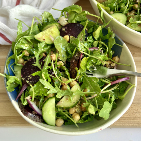 Blue and white bowl with salad inside with beets, chickpeas and cucumber with a fork piercing the salad and another white bowl with salad on the side.