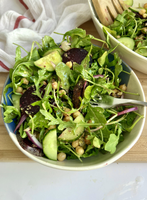 Blue and white bowl with salad inside with beets, chickpeas and cucumber with a fork piercing the salad and another white bowl with salad on the side.