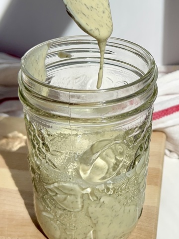 Mason jar with tahini dressing inside with a spoon dripping salad dressing off it.