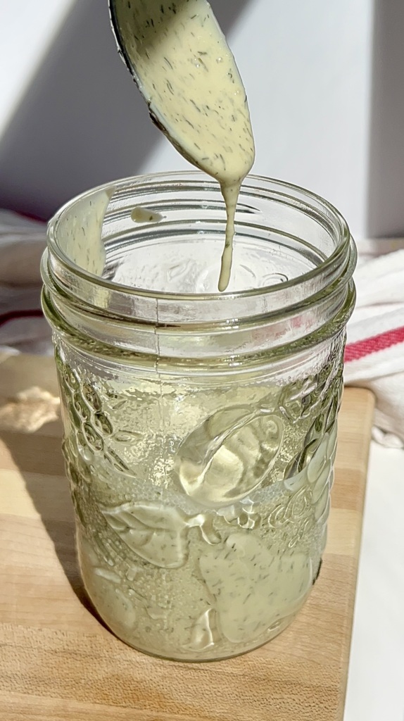 Mason jar with tahini dressing inside with a spoon dripping salad dressing off it.