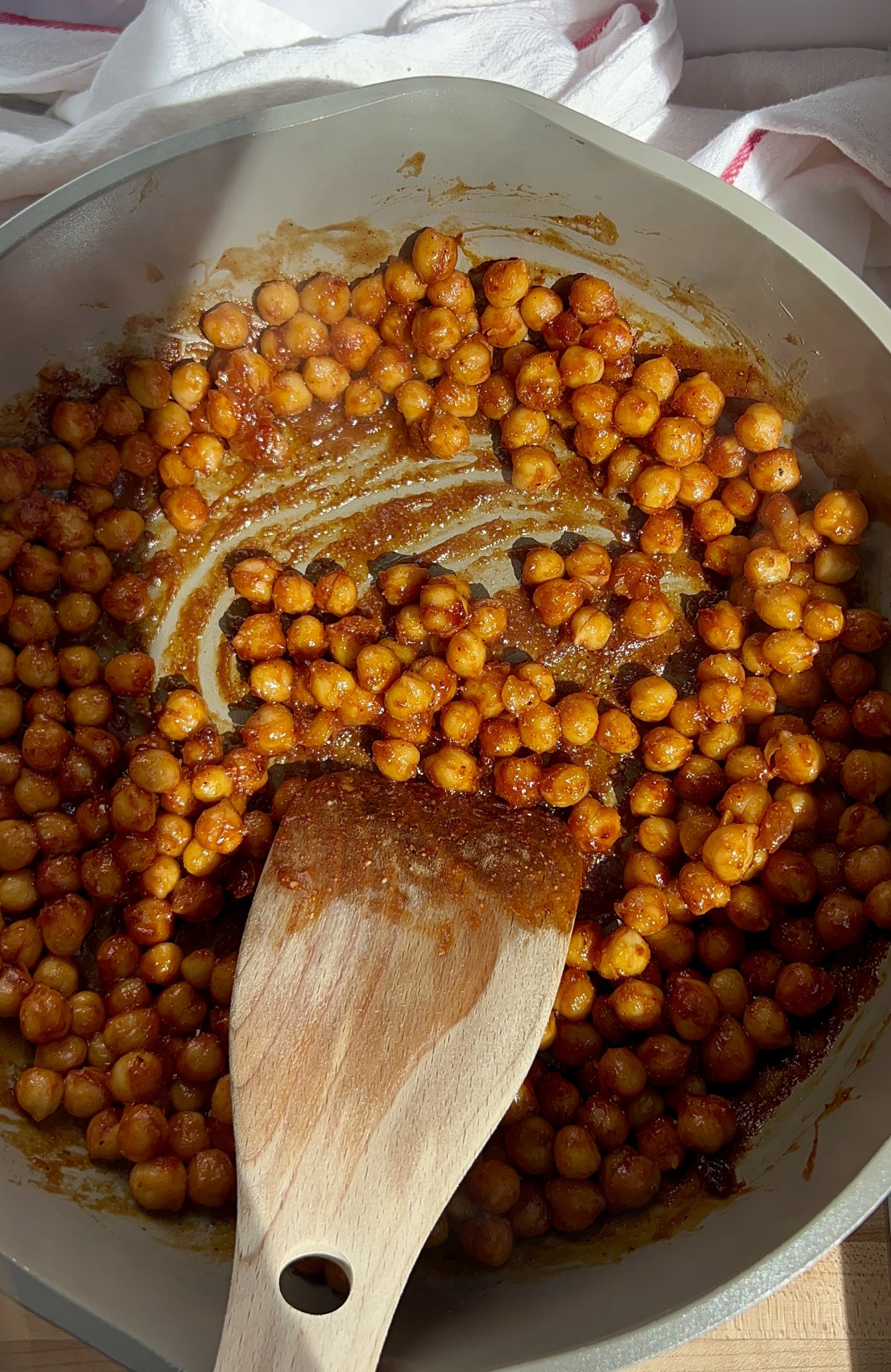 Pan with chickpeas covered in BBQ sauce with a spatula sautéing them.