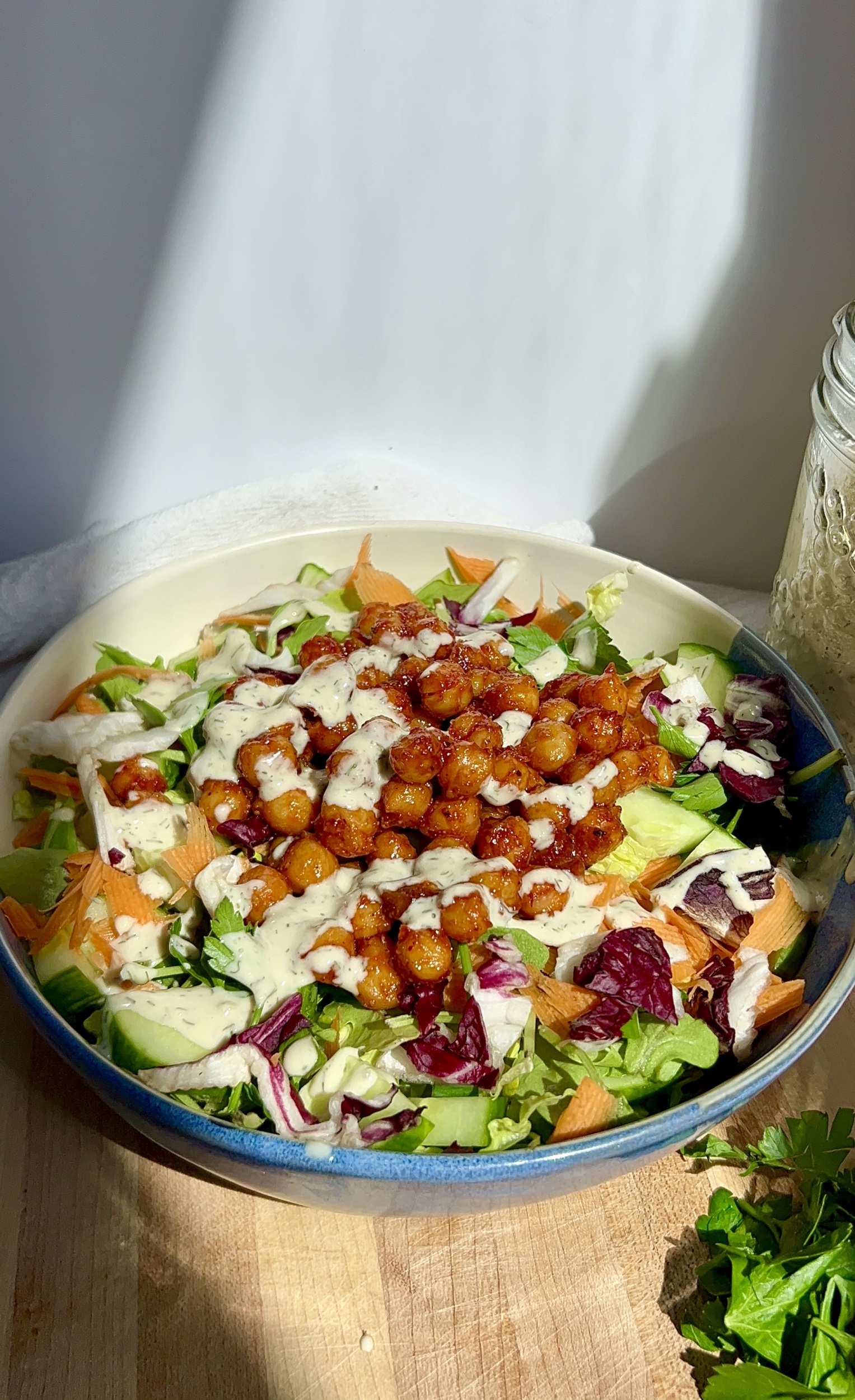 Bowl with salad in it with BBQ chickpeas inside drizzled with vegan tahini ranch.