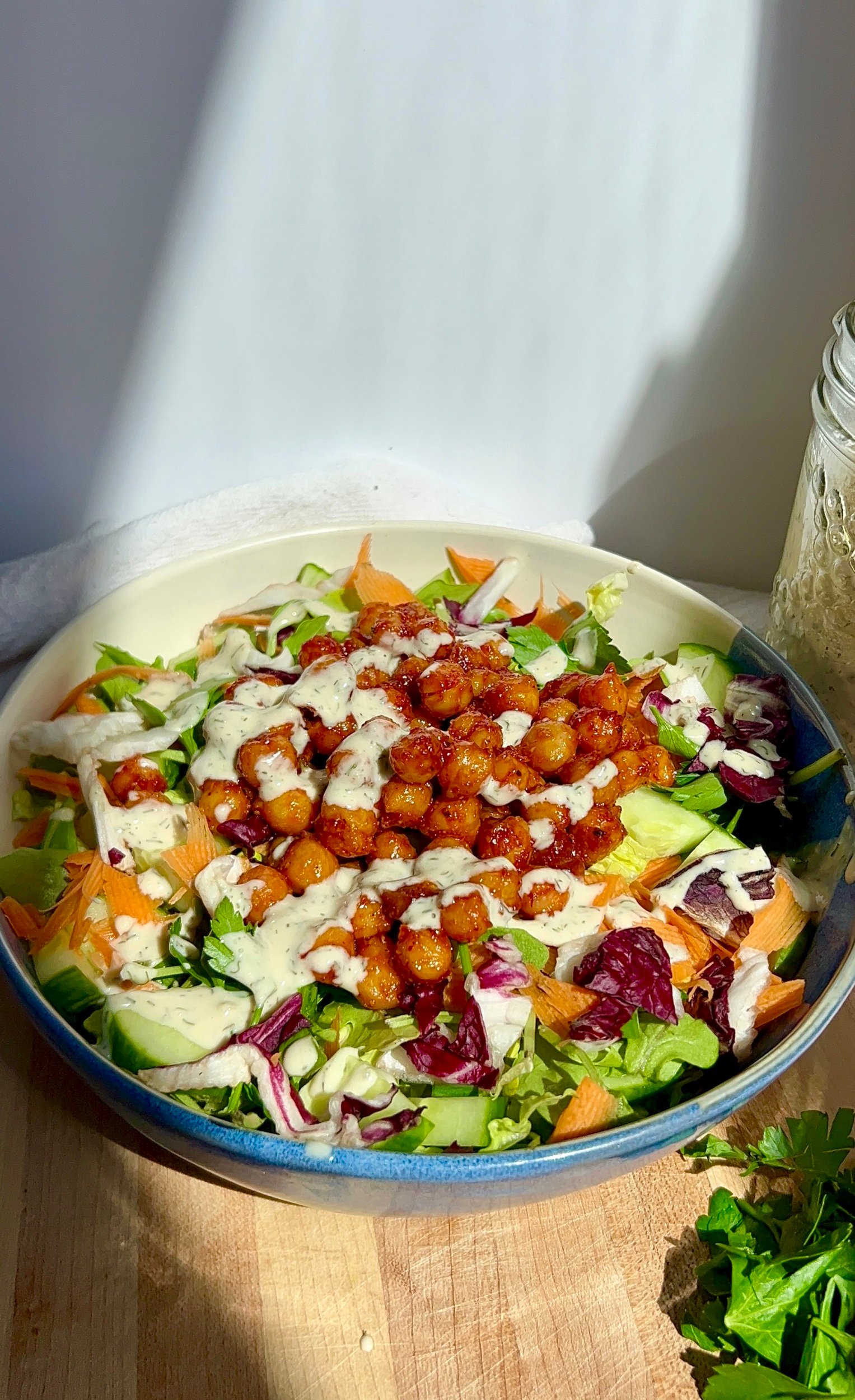 Bowl with salad in it with BBQ chickpeas inside drizzled with vegan tahini ranch.