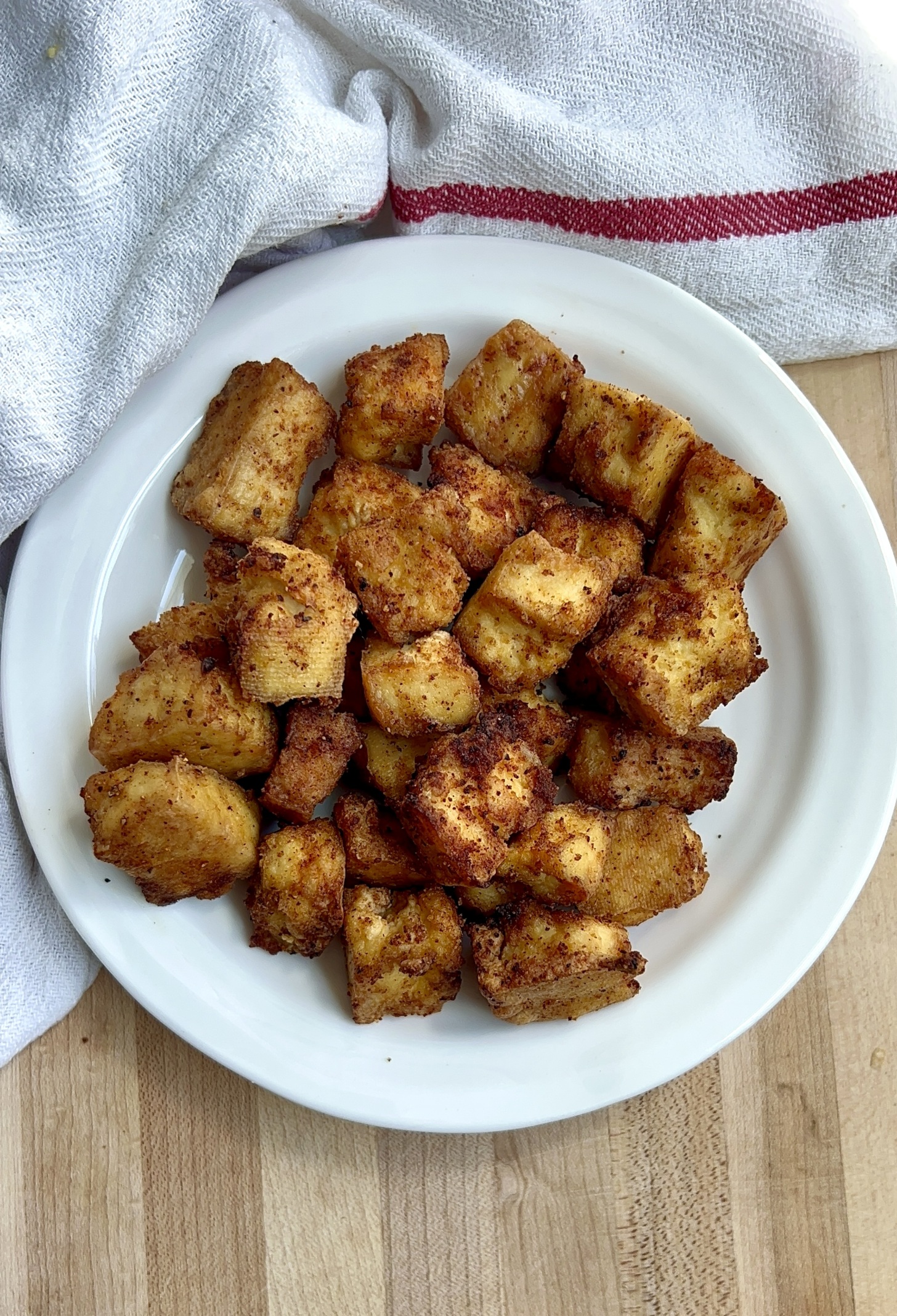 Golden brown tofu on a white plate on a cutting board