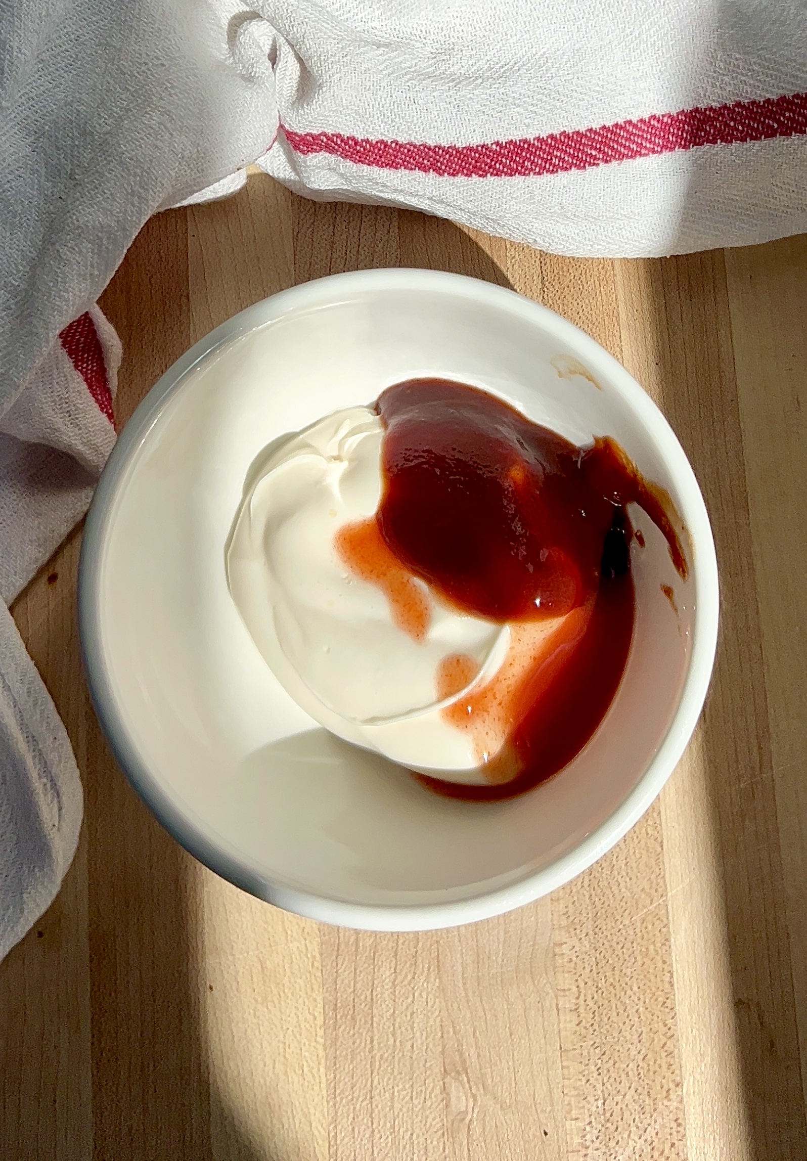 White bowl with mayo inside and barbecue sauce.